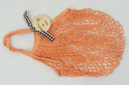 Bolsa de playa antiarena en color naranja con accesorio decorativo de madera circular.
