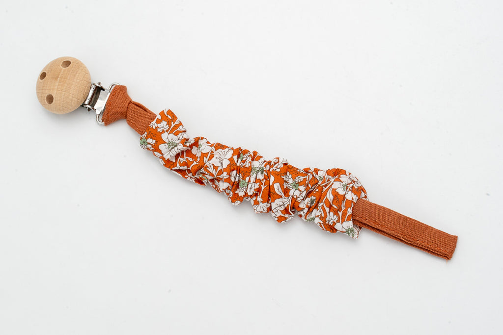 Attache-tétine en tissu froncé à fleurs sur fond terracotta avec clip en bois
