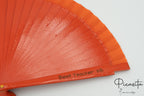 Détail d’un éventail en bois couleur corail avec une dédicace pour une enseignante gravée sur un brin
