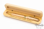 Bolígrafo de madera con detalles dorados dentro de un estuche de bambú abierto con grabado personalizado.