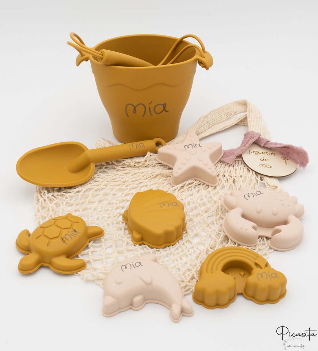 Cubo de playa color mostaza personalizado con nombre láser y bolsa de malla beige.