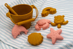 Variedad de moldes marinos en silicona colores mostaza y rosa sobre fondo rayado.