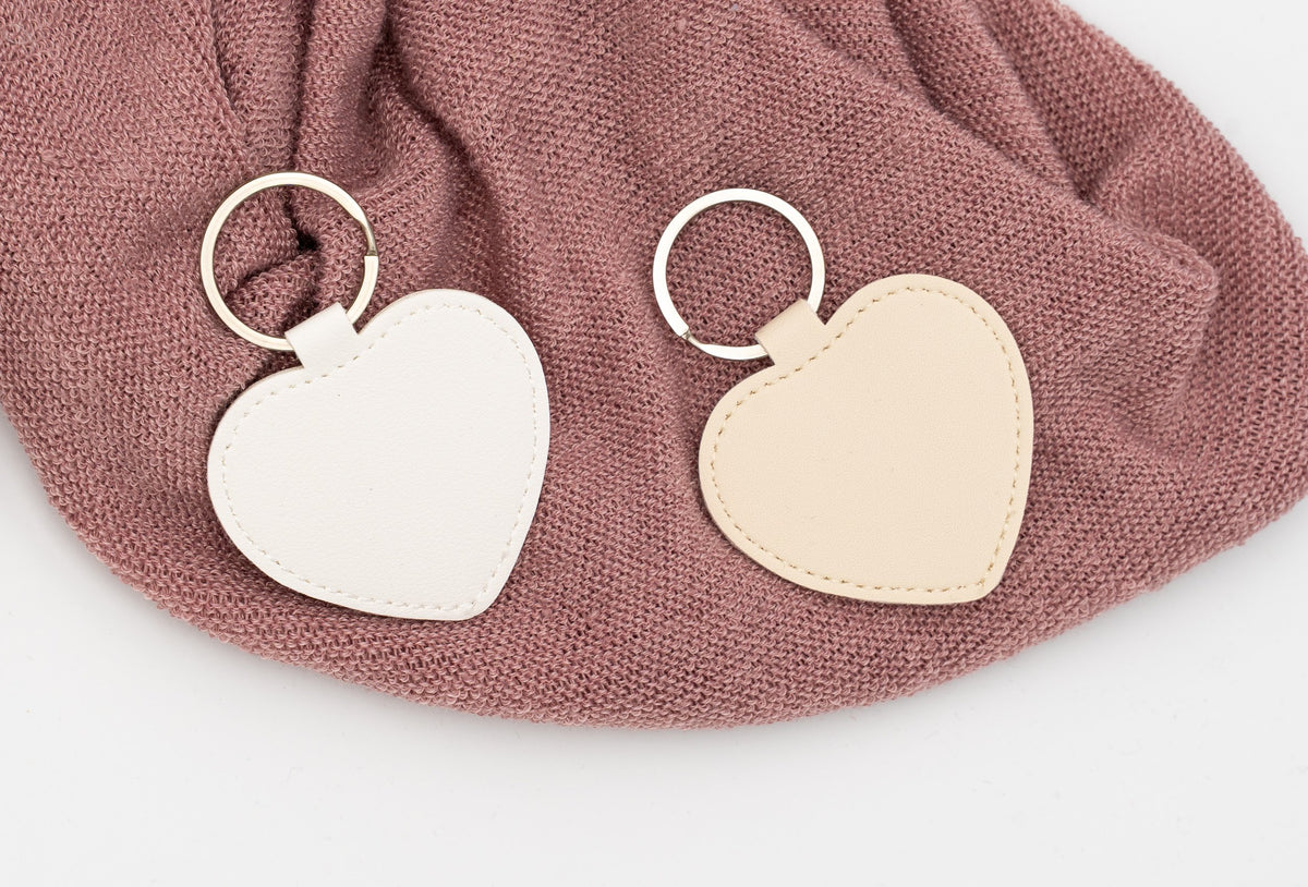 Porte-clés cœur blanc et beige non personnalisés sur un tissu rose.