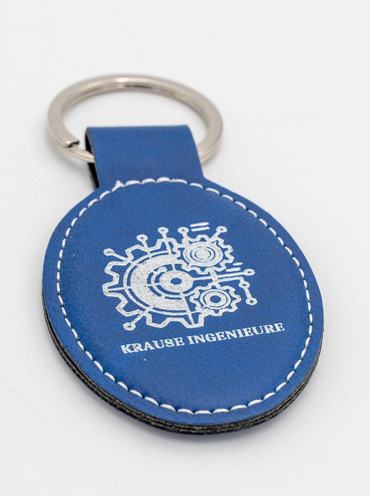 Porte-clé ovale bleu avec logo clair et couture blanche.