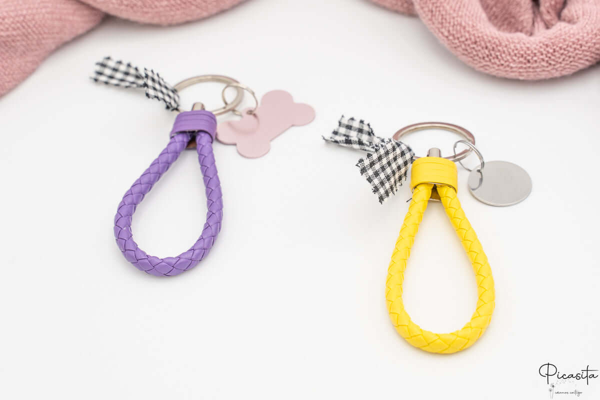 Detalle de llavero trenzado amarillo con chapa circular y llavero púrpura con chapa de hueso.
