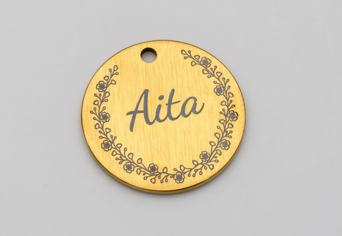 Médaille dorée avec le nom Aita gravé dans une bordure de fleurs
