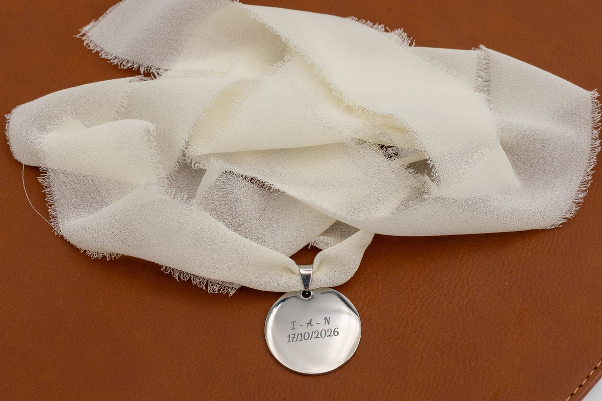 Médaille argentée avec initiales et date gravées sur un ruban en mousseline ivoire