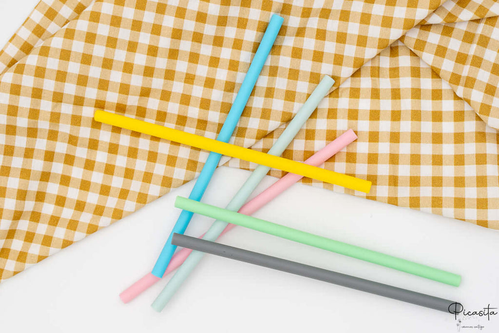 Pajitas reutilizables cruzadas sobre un fondo blanco y textil de cocina.
