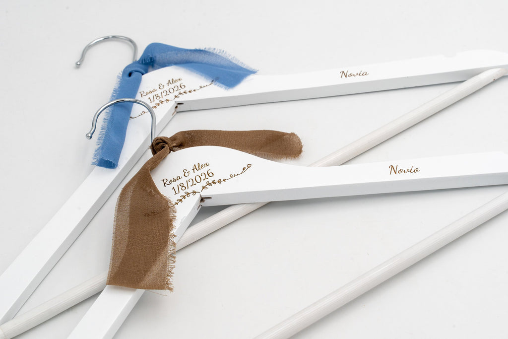 Deux cintres blancs pour les mariés avec prénoms et date gravés et des nœuds en mousseline bleus et marron