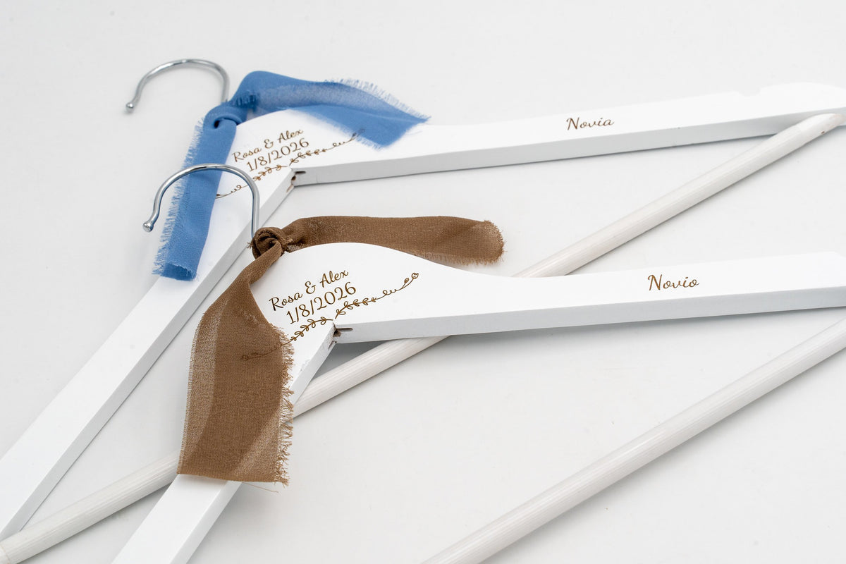Deux cintres blancs pour les mariés avec prénoms et date gravés et des nœuds en mousseline bleus et marron