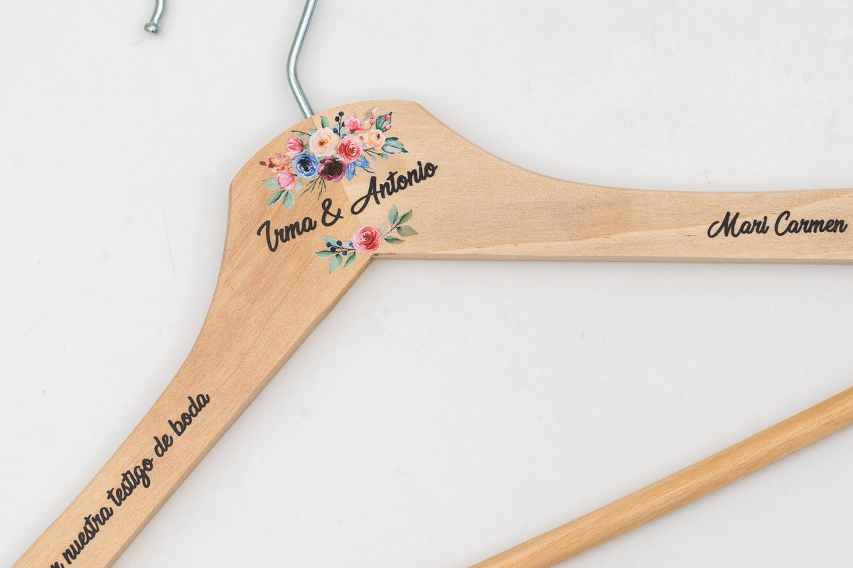 Cintre en bois clair personnalisé avec prénoms et fleurs, détail de l'épaule.