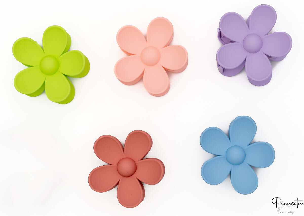 Cinco pinzas para el pelo con forma de flor en colores variados dispuestas sobre fondo blanco.