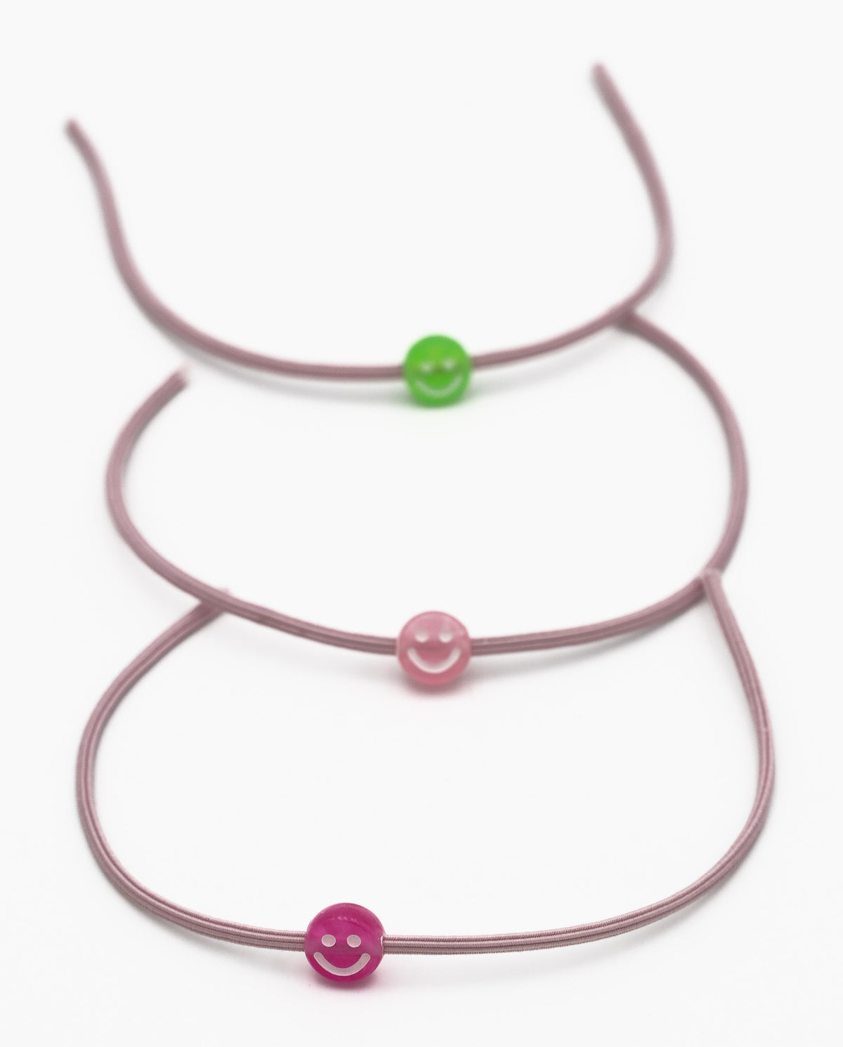 Trois bracelets élastiques mauves avec perles en silicone en forme de sourire vertes et roses