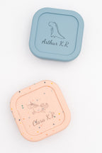 Deux boîtes moyennes, bleue et rose mouchetée, avec les prénoms Arthur K.R et Clara K.R et un dinosaure et une licorne gravés