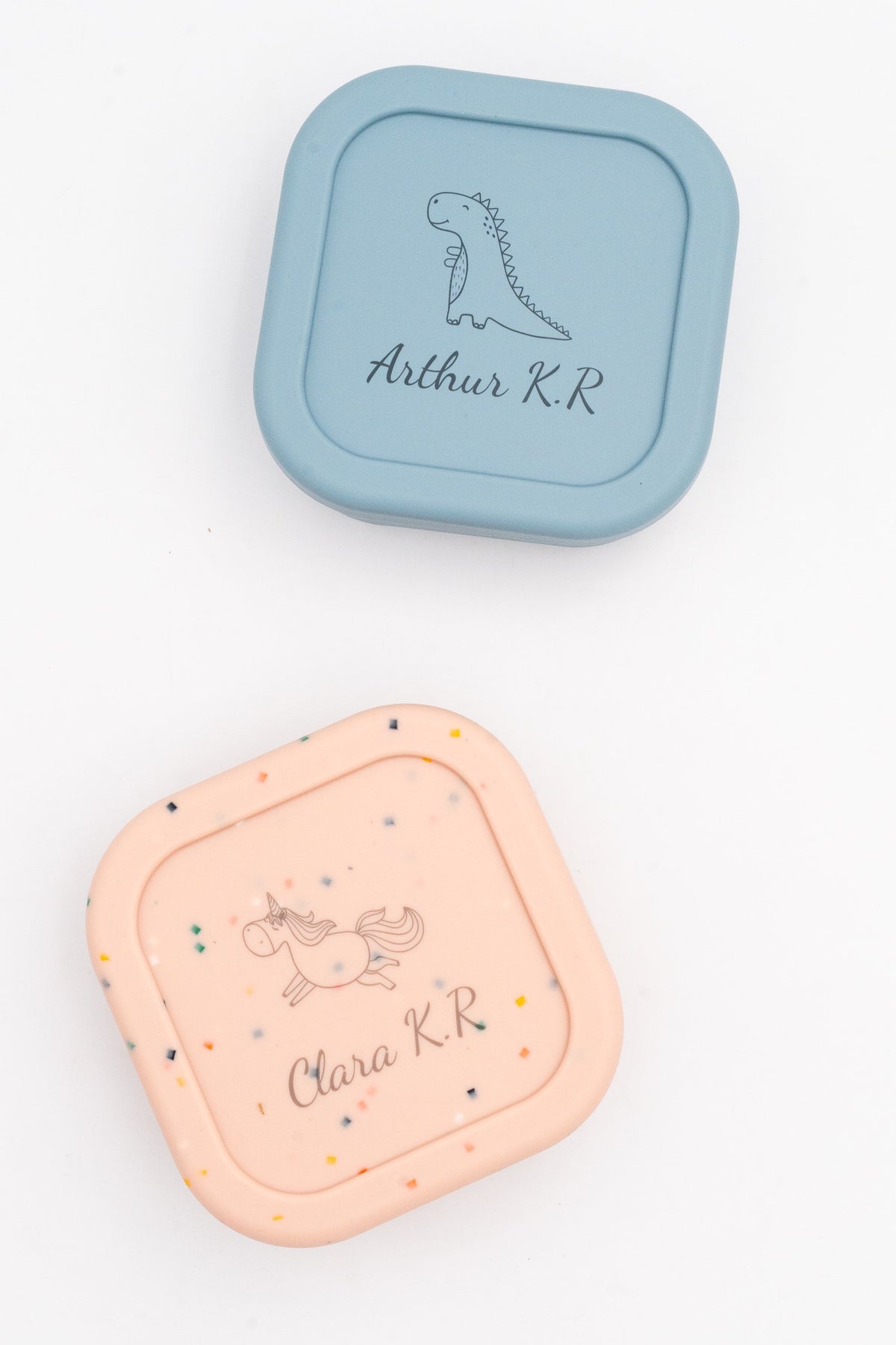 Deux boîtes moyennes, bleue et rose mouchetée, avec les prénoms Arthur K.R et Clara K.R et un dinosaure et une licorne gravés